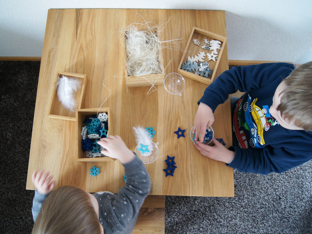 Weihnachtskugeln mit Kleinkindern dekorieren. Streuteile, Weihnachtsdeko und Federn kombinieren und in die Glaskugel füllen. Basteln mit Kindern von Fantasiewerk