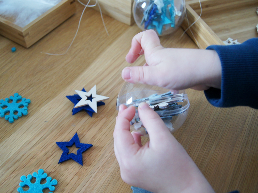 Weihnachtskugeln mit Kleinkindern dekorieren. Streuteile, Weihnachtsdeko und Federn kombinieren und in die Glaskugel füllen. Basteln mit Kindern von Fantasiewerk